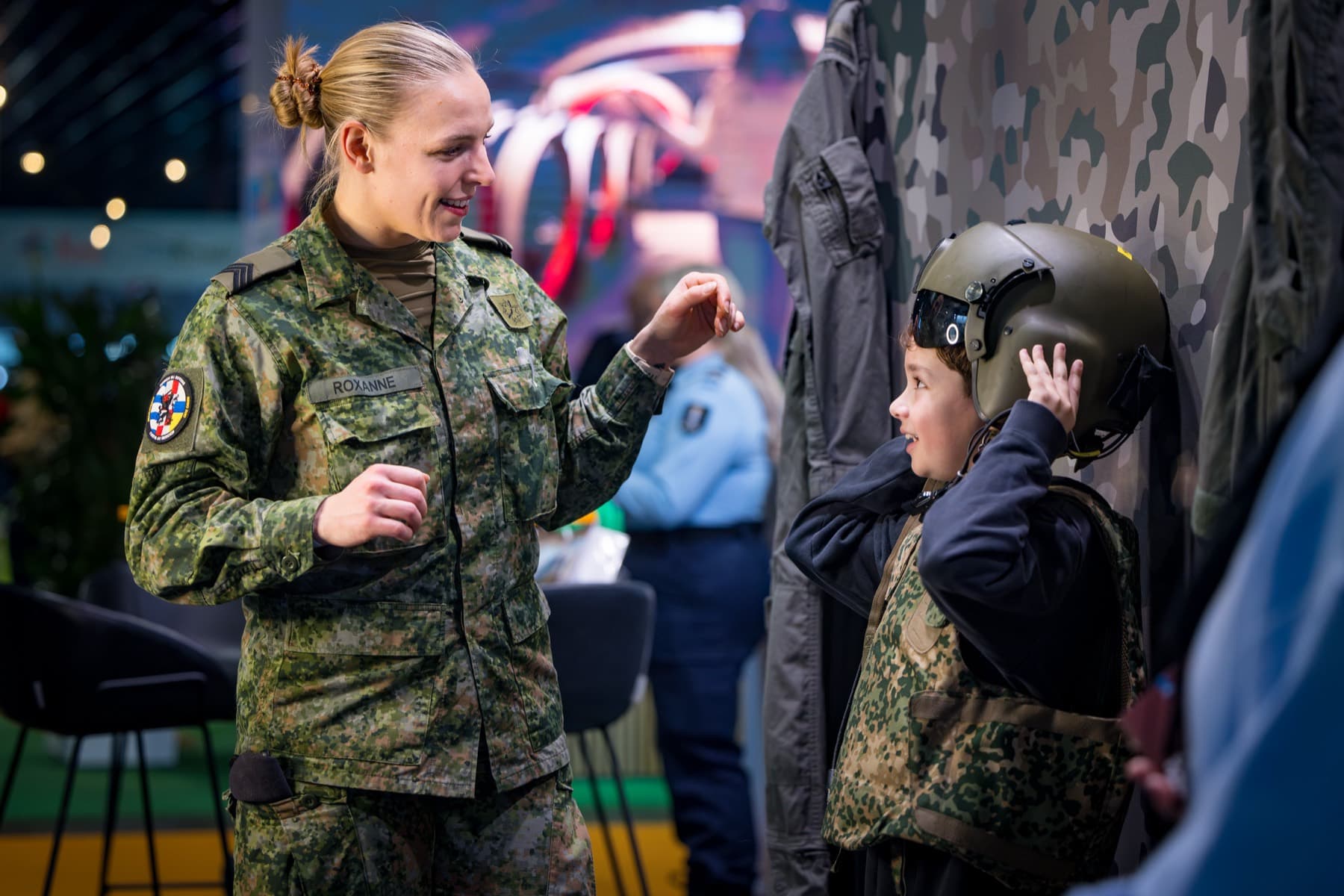 Militair helpt een kind een vliegeniershelm passen op een defensiebeurs