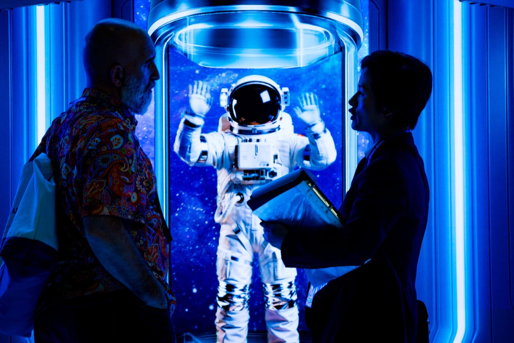 Bezoekers bij een verlichte astronaut-installatie in blauw licht