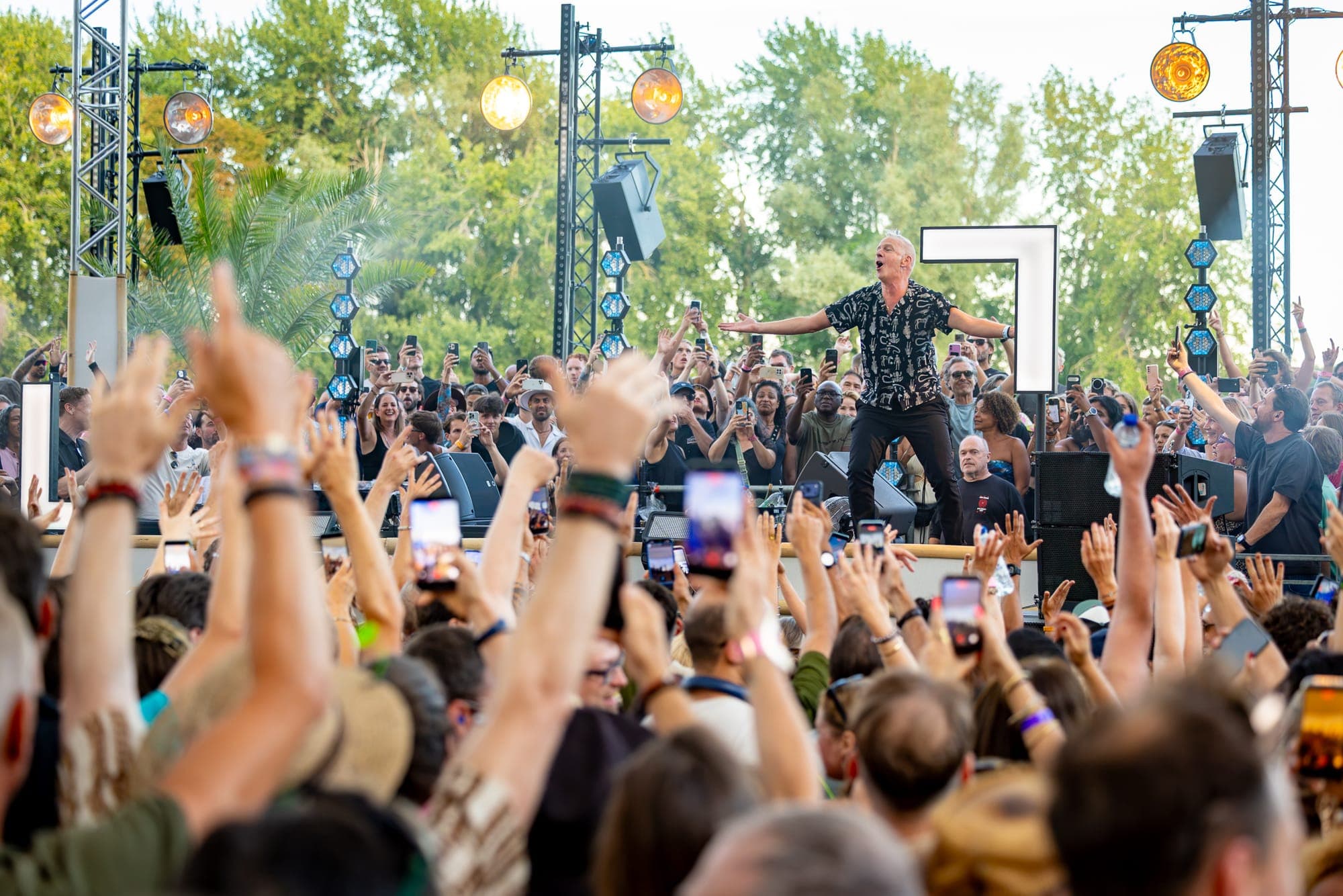 DJ with arms spread on stage at LoveLand Festival, crowd with raised hands and phones