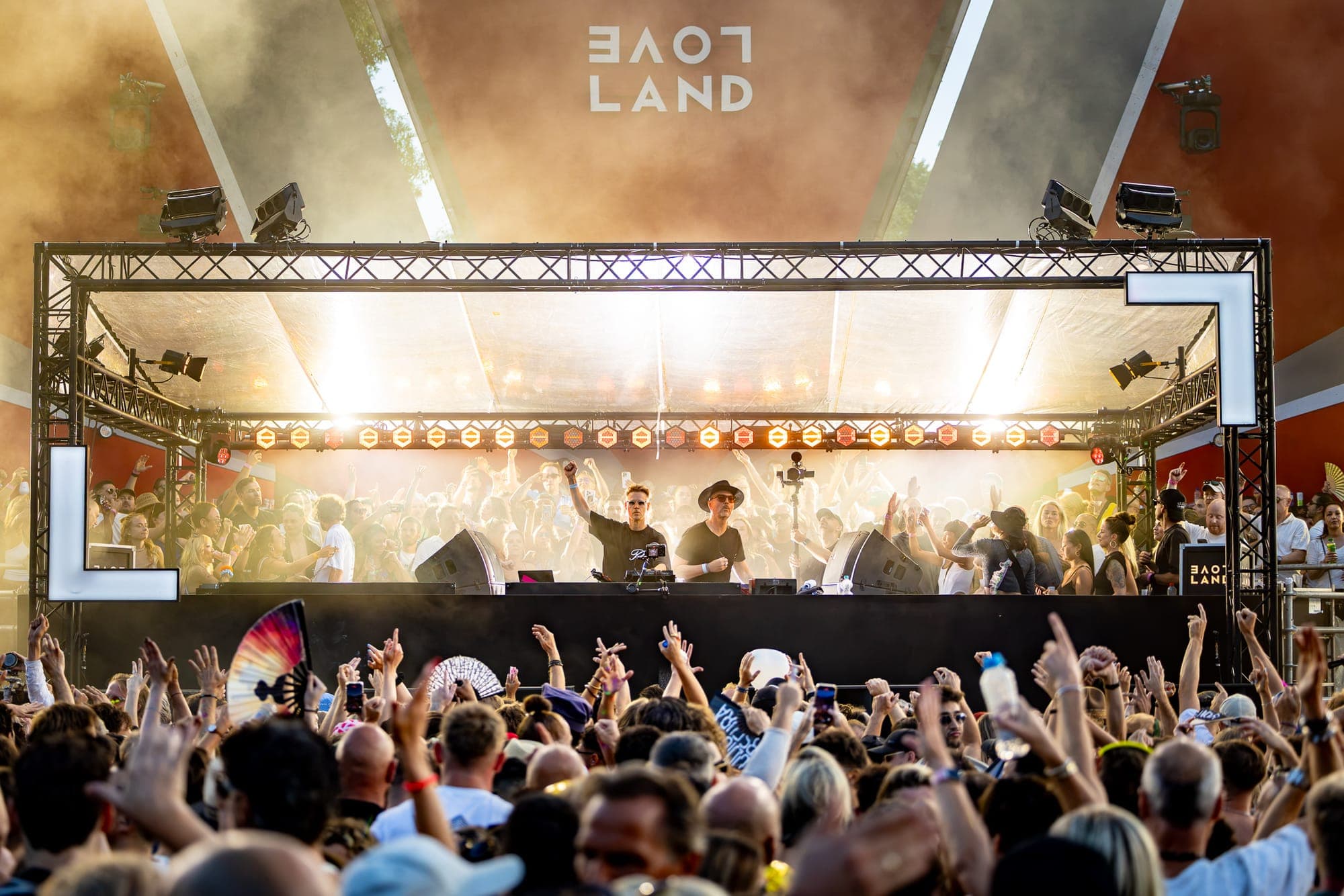 Two DJs behind the decks under the LoveLand stage canopy, backlit by the evening sun